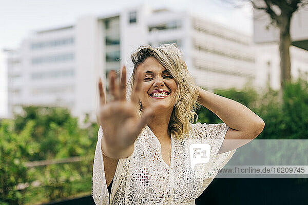 Lächelnde junge Frau mit Hand im Haar  die eine Stopp-Geste zeigt