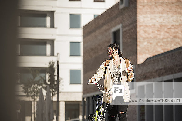 Lächelnde Studentin  die wegschaut  während sie mit dem Fahrrad gegen ein Gebäude fährt