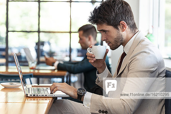 Junger Geschäftsmann trinkt Kaffee und benutzt einen Laptop in einem Café