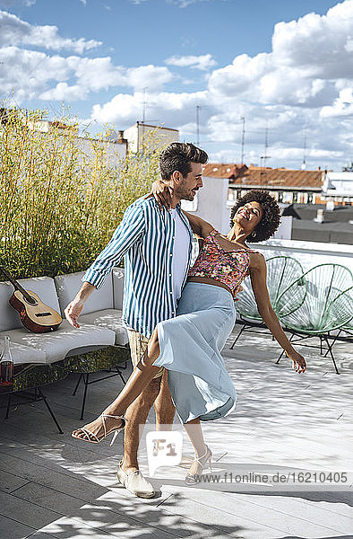Multi-ethnisches Paar tanzt auf der Penthouse-Terrasse an einem sonnigen Tag