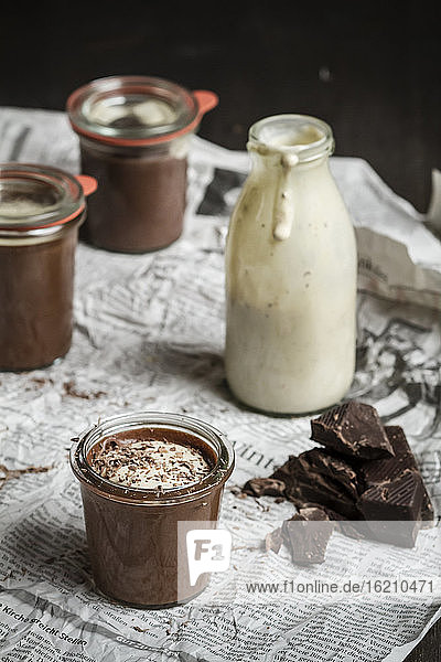 Gläser mit Schokoladenpudding und Vanillesauce in einer Flasche auf einer Zeitung  Nahaufnahme
