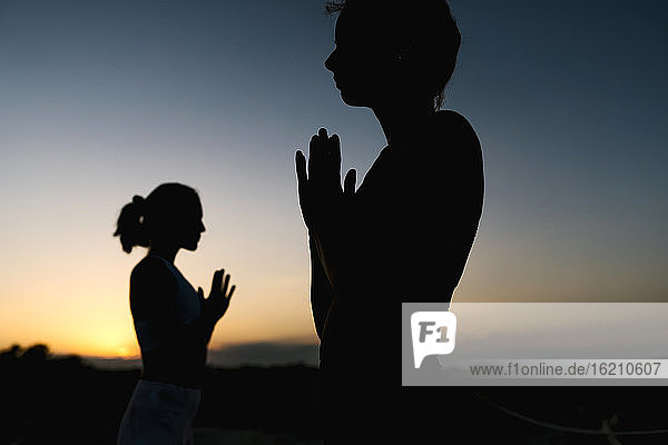 Silhouette Frauen in Gebetshaltung bei Sonnenuntergang