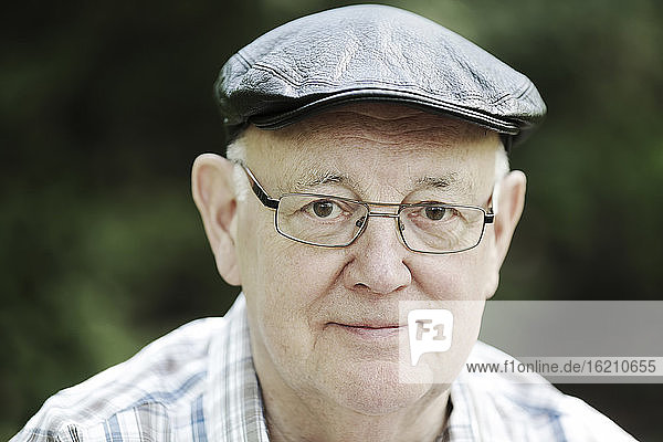 Deutschland  Nordrhein-Westfalen  Köln  Porträt eines älteren Mannes mit Mütze und Brille im Park  lächelnd