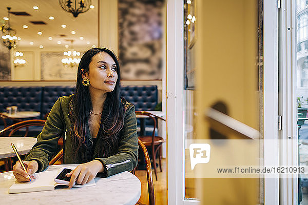 Junge Frau  die im Café in ein Buch schreibt und nach draußen schaut