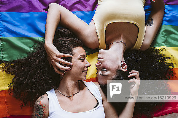 Romantic lesbian couple looking at each other while lying on rainbow flag