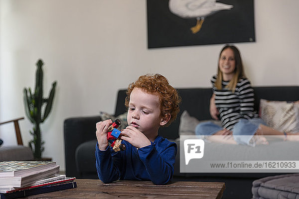 Mutter entspannt sich auf dem Sofa  während ihr Sohn mit einem Spielzeugroboter auf dem Tisch zu Hause spielt