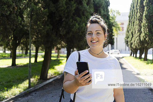 Porträt einer lächelnden kurvenreichen jungen Frau mit Handy in einem öffentlichen Park