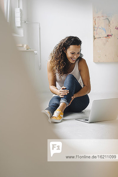 Lächelnde Frau  die zu Hause auf dem Boden sitzend ein Video über einen Laptop betrachtet