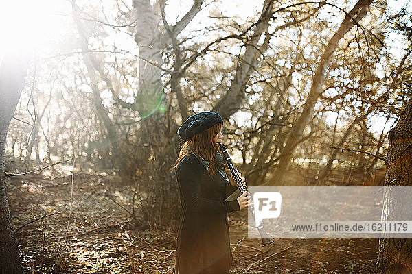 Junge rothaarige Frau spielt Klarinette beim Üben im Wald