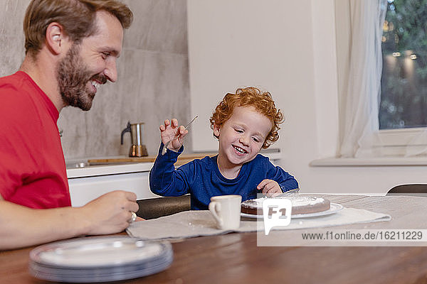 Glücklicher Vater und Sohn betrachten einen Schokoladenkuchen auf dem Esstisch in der Küche