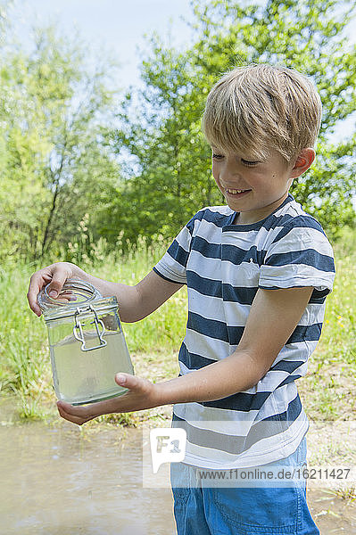 Deutschland  Bayern  München  Junge füllt Wasser in Glasgefäß am See  lächelnd