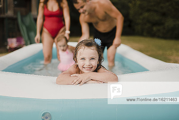 Porträt eines glücklichen Mädchens in einem aufblasbaren Schwimmbecken mit Familie im Hintergrund