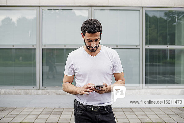 Gut aussehender Mann im mittleren Erwachsenenalter  der ein Smartphone benutzt  während er auf dem Fußweg vor einem Gebäude steht