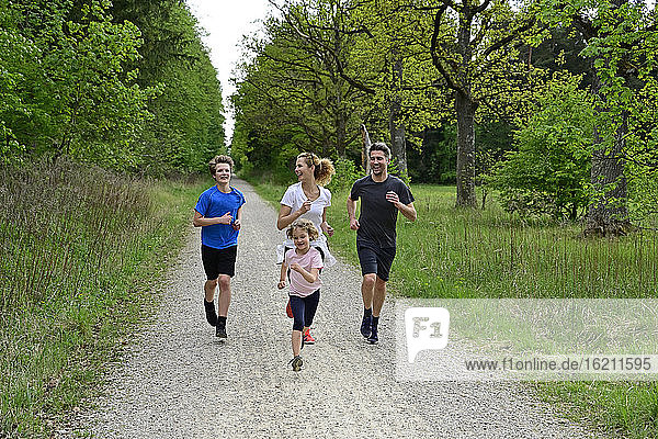 Fröhliche Familie läuft auf unbefestigtem Weg inmitten von Bäumen und Pflanzen im Wald