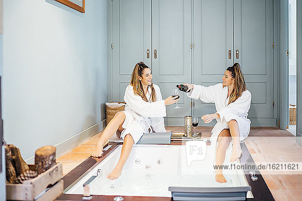 Zwillingsschwestern genießen Wein  während sie am Whirlpool im Hotelzimmer sitzen