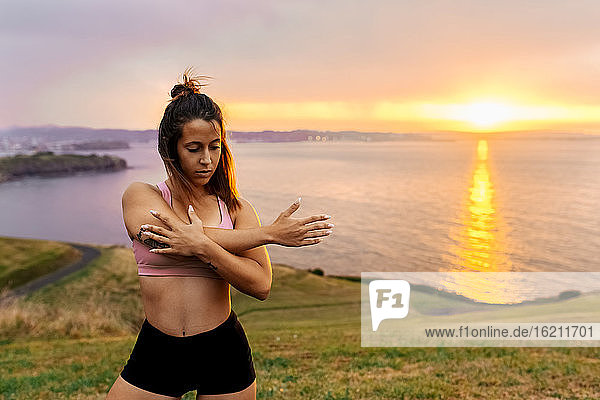 Schöne weibliche Athletin  die sich bei Sonnenuntergang auf dem Meer stehend dehnt