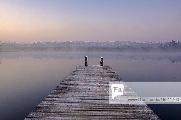 Jetty on shore of Kirchsee lake at foggy dawn