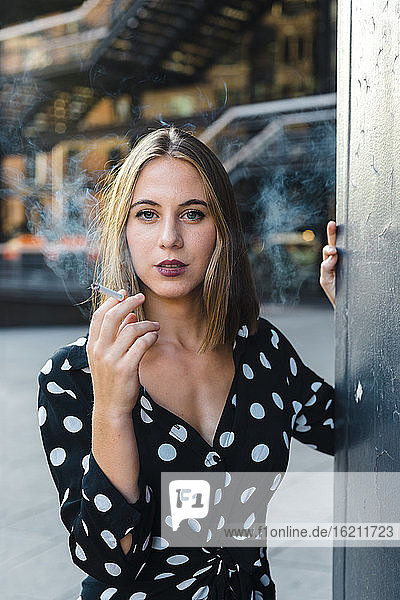 Beautiful woman smoking cigarette while standing in city