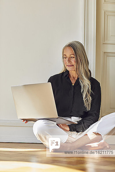 Frau benutzt Laptop  während sie zu Hause auf dem Boden sitzt