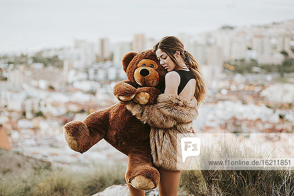 Frau mit geschlossenen Augen  die einen Teddybär umarmt  während sie vor der Stadt steht