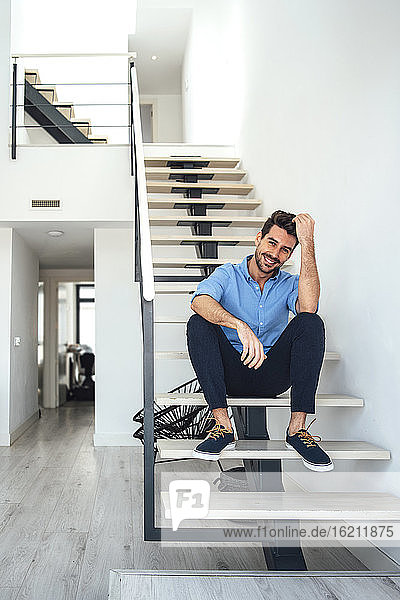 Glücklicher Mann sitzt auf einer schwebenden Treppe in einem modernen Penthouse