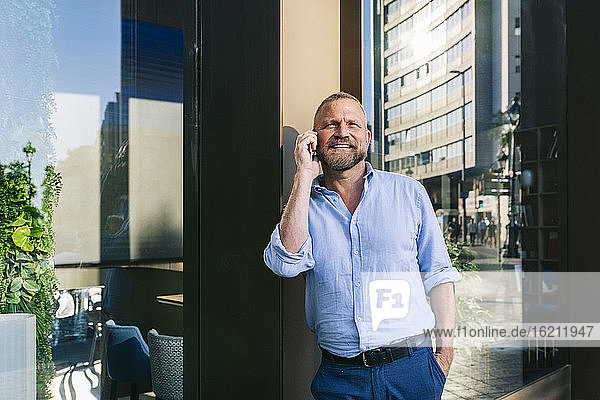 Smiling businessman talking on mobile phone while leaning on wall