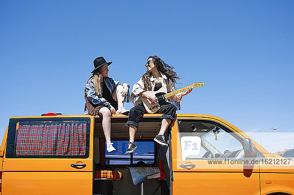 Zwei Frauen sitzen auf dem Dach eines Lieferwagens und spielen Gitarre
