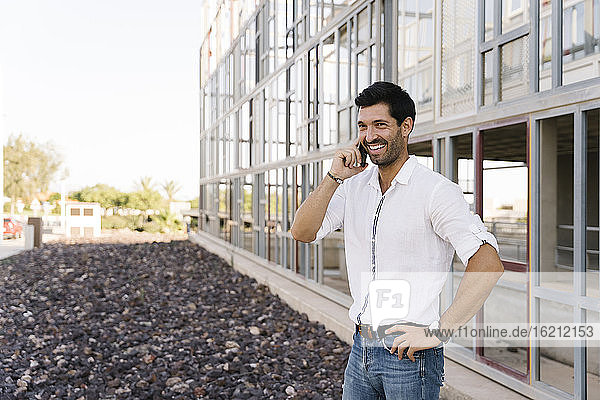 Smiling businessman talking on phone outside building