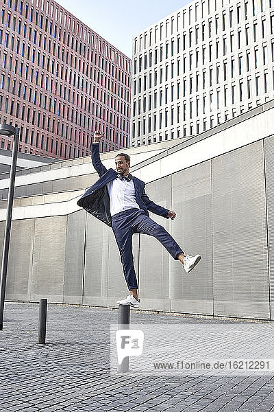 Happy businessman balancing on pole in city