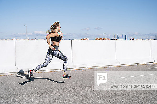 Mid erwachsene Frau läuft auf der Straße gegen den blauen Himmel in der Stadt während des sonnigen Tages
