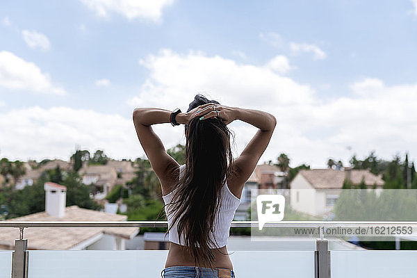 Mittlere erwachsene Frau bindet sich die Haare  während sie auf einem Balkon steht