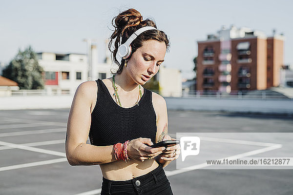 Woman wearing headphone using mobile phone outdoors
