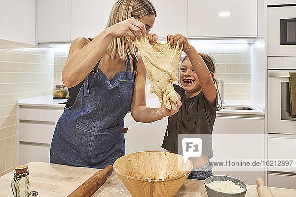 Mutter mit fröhlicher Tochter knetet Pizzateig in der Küche zu Hause