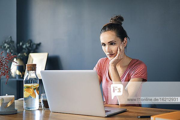 Unternehmerin mit Laptop auf dem Schreibtisch an der Wand im Heimbüro