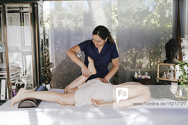 Female therapist giving leg massage to customer relaxing on table in spa
