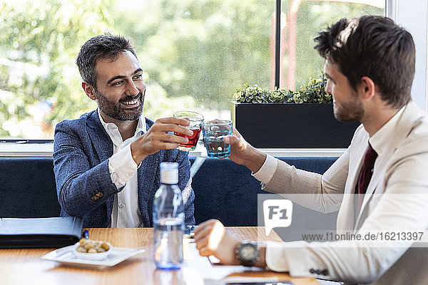 Businessmen toasting drinks while sitting at table in cafe