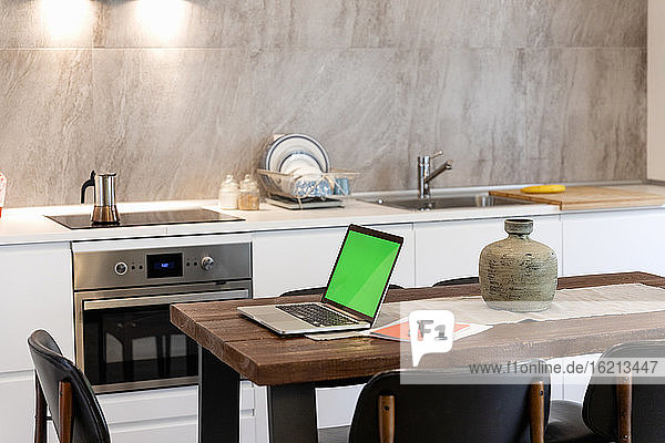 Laptop und Smartphone auf dem Esstisch in der modernen Küche zu Hause