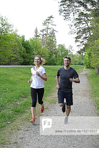 Glückliches Paar joggt auf unbefestigtem Weg gegen Bäume im Wald