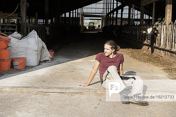Junger Bauer auf dem Boden sitzend im Kuhstall auf einem Bauernhof