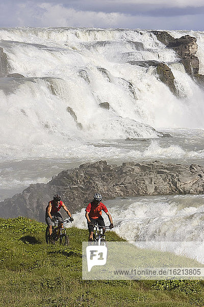 Island  Männer beim Mountainbiking  Wasserfall im Hintergrund