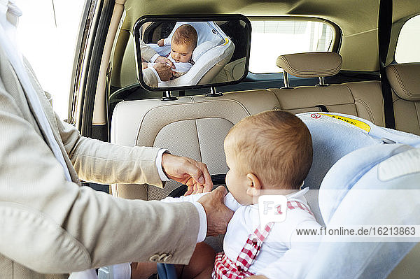 Father fastening baby boy sitting in child's seat in a car