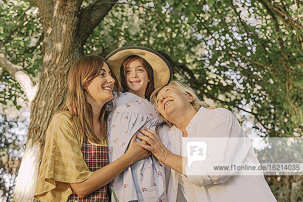 Glückliche Familie umarmt Mädchen mit Hut vor einem Baum im Garten