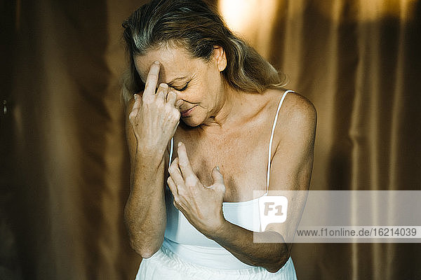 Senior woman touching her forehead against curtain