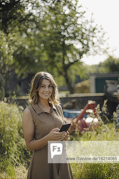 Porträt einer lächelnden jungen Frau mit Mobiltelefon auf dem Lande