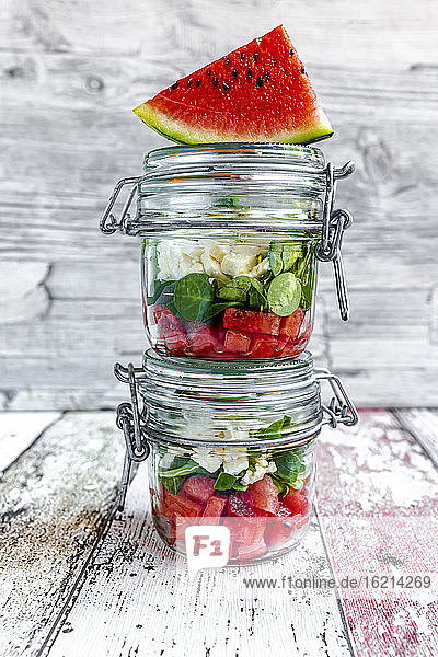 Wassermelonenscheiben und Gläser mit Wassermelonensalat mit Fetakäse  Feldsalat und Minze