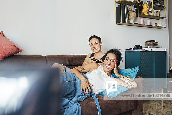 Smiling lesbian couple watching TV on sofa