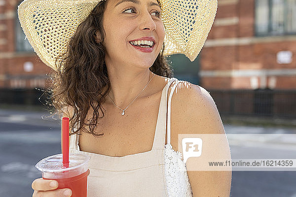 Nahaufnahme einer glücklichen jungen Frau mit Hut und Getränk in der Stadt