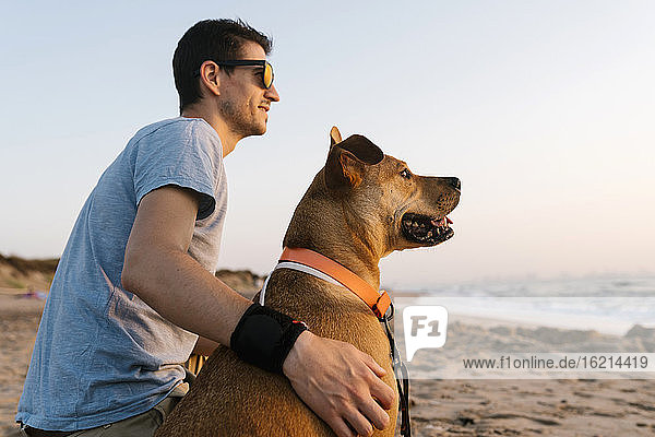 Mann und Hund schauen weg  während sie am Strand sitzen