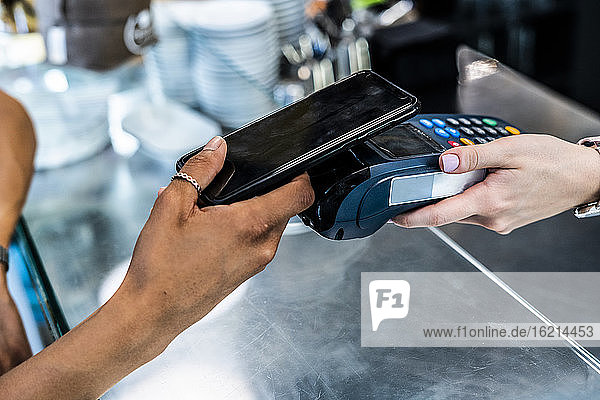 Kundin beim kontaktlosen Bezahlen mit dem Smartphone in einem Café