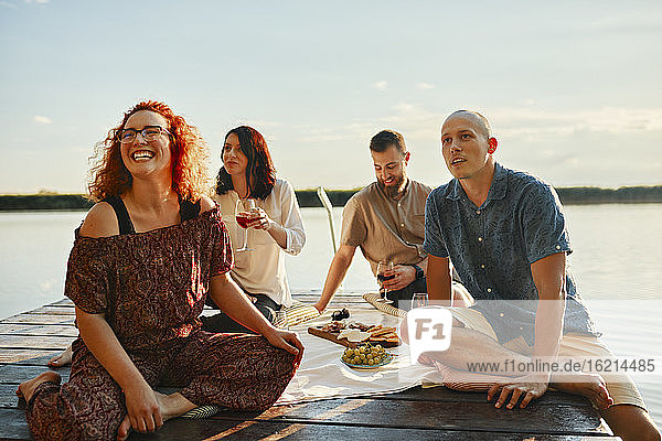 Glückliche Freunde beim Picknick auf einem Steg an einem See bei Sonnenuntergang